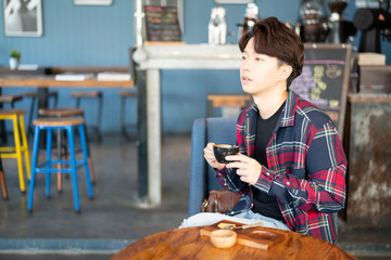Handsome young asian man holding a cup of coffee and drinking coffee while sitting in the rest area of the coffee shop.