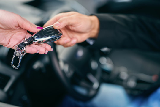 Close up of woman giving car keys to man in car. Selective focus on hands.