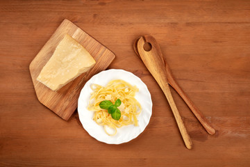 A photo of a plate of Italian pasta with Parmesan cheese and basil leaves, shot from the top on a dark rustic wooden background with a place for text