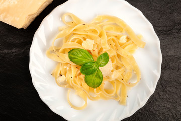 An overhead closeup photo of a plate of Italian pasta with Parmesan cheese and basil leaves