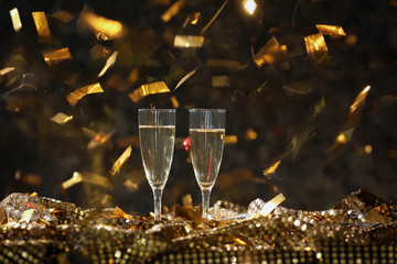 Glasses of champagne with falling confetti on dark background