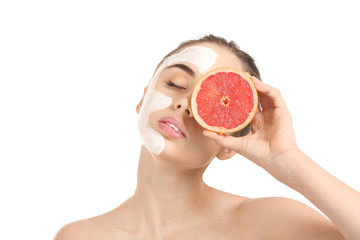 Beautiful young woman with facial mask and grapefruit on white background