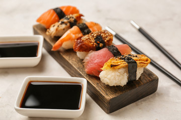 Board with tasty sushi with sauce on light table