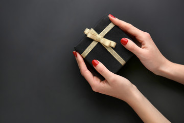 Female hands with manicure holding gift box on dark background