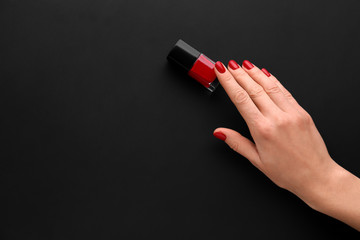 Female hand with bottle of nail polish on dark background - obrazy, fototapety, plakaty
