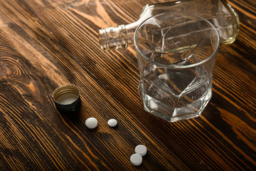 Empty glass and bottle with pills on wooden table. Concept of alcoholism