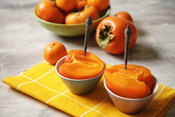 Bowls with cut ripe persimmons on grey table