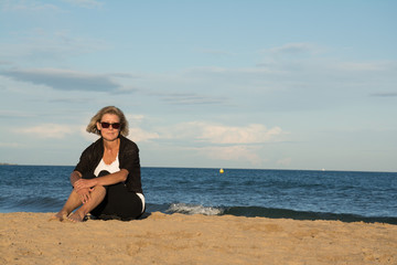 Frau am Strand mit Sonnenbrille sitzend