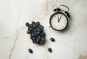 Ripe sweet grapes and alarm clock on light table