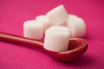  closeup of sugar in shaped circle in red spoon on pink background