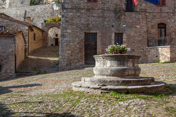 Fototapeta na wymiar A travertine well in the centre of ancient square named after the painter Vecchietta in medieval town of Castiglione d'Orcia, Italy