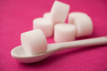  closeup of sugar in shaped circle in white spoon on pink background