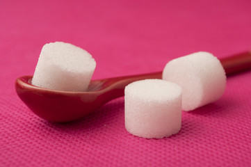  closeup of sugar in shaped circle in red spoon on pink background