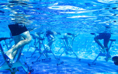 Touristen doing aqua aerobics on exercise bikes in swimming pool tropical hotel
