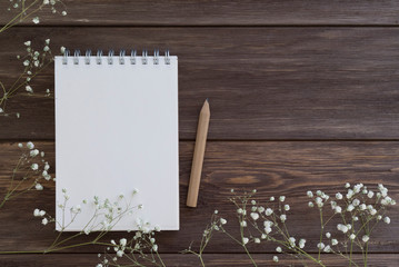 Notebook with pencil and little white flowers on the wooden background. Spring and Mother's Day concept. Top view, copy space, mock up