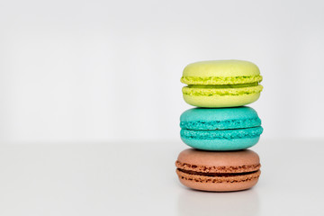 Green, turquoise and brown french macarons on the white table. Close-up, front view, copy space