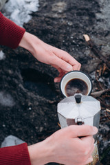 Traveling man a sits near camp fire an in winter time and pours itself hot coffee . Concept adventure active vacations outdoor. Winter camping