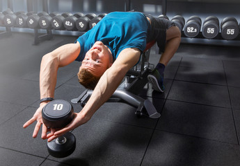 Fototapeta na wymiar guy doing exercise in the gym. young man holding a 10 kg dumbbell, and he is lying on his back