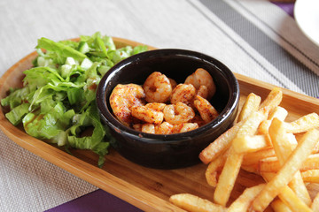 Fried shrimp with spices, deep-fried potatoes and greens on a wooden plate