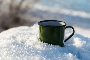 Drinking tea in the winter outdoors. Mug of hot tea in the snow, morning tea outdoors in the rays of the winter sun.