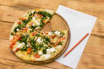 Count the calories. Sheet with the inscription Calories and lying near a pizza on a wooden background.