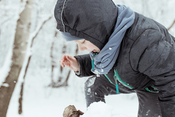 A little boy of 5-7 years old is playing outside in the snow in a park in winter.