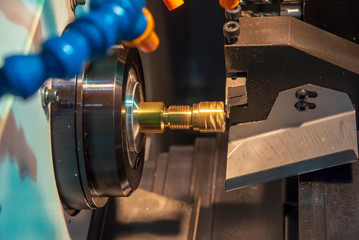 The CNC lathe or turning machine cutting the thread  at the brass  shaft.Hi-technology manufacturing process.