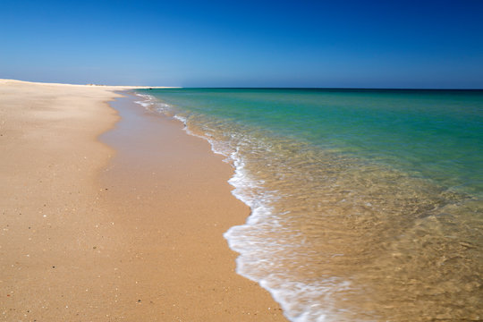 Empty white sand beach and breaking waves of crystal clear sea, Ilha do Farol, Culatra barrier island, Olhao, Algarve, Portugal