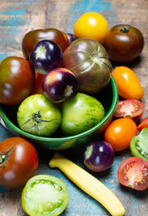 Multicolored assortment of French fresh ripe tomatoes in green bowl on blue wooden table