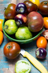 Multicolored assortment of French fresh ripe tomatoes in green bowl on blue wooden table