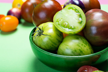 Multicolored assortment of French fresh ripe tomatoes in green bowl on green table