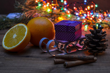 Box with a gift on a sled. Cone, oranges, Christmas lights. The aroma of the winter holidays - luminous garland.