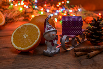 The original festive picture is a figure of a snowman who drags a sleigh with a gift, around oranges, Christmas lights, a pine cone, cinnamon sticks. The aroma of the winter holidays.