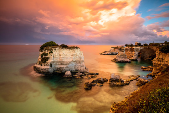 Sunset frames the high cliffs known as Faraglioni di Sant'Andrea and the turquoise sea province of Lecce Apulia Italy Europe