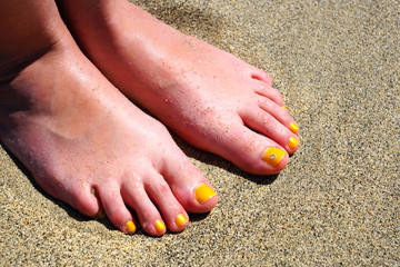 Pair of bare feet with yellow nail polish and a toe crystal at the beach