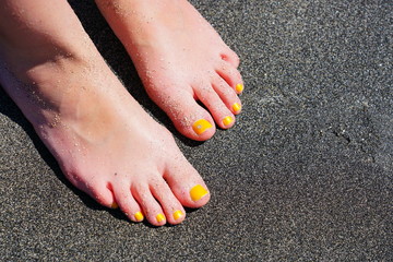 Pair of bare feet with yellow nail polish and a toe crystal at the beach