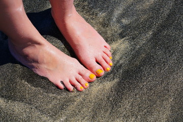 Fototapeta na wymiar Pair of bare feet with yellow nail polish and a toe crystal at the beach