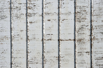 A white wall with a rough texture of a large industrial building with ribs and scuffs to the concrete. Background