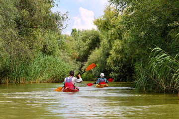 Rear view of people in two kayaks. Kayaking on summer Danube river together with green trees in the background. Concept of tourism and outdoor activities on the water