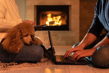 Couple of freelancers siting at the floor with a laptop and tablet. On the fireplace background. 
