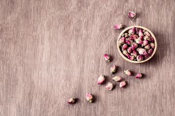 Pink red dried rose buds in wooden bowl with petals on old wooden background copyspace top view.