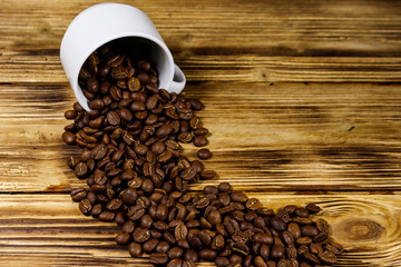 Roasted coffee beans spill out of cup on wooden table