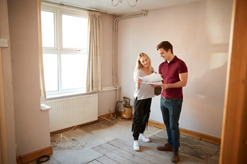 Couple Buying House For First Time Looking At House Survey In Room To Be Renovated