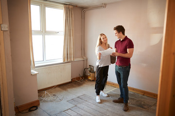 Couple Buying House For First Time Looking At House Survey In Room To Be Renovated