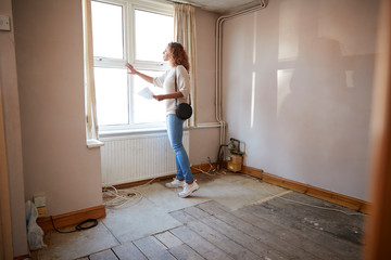 Fototapeta na wymiar Female First Time Buyer Looking At House Survey In Room To Be Renovated