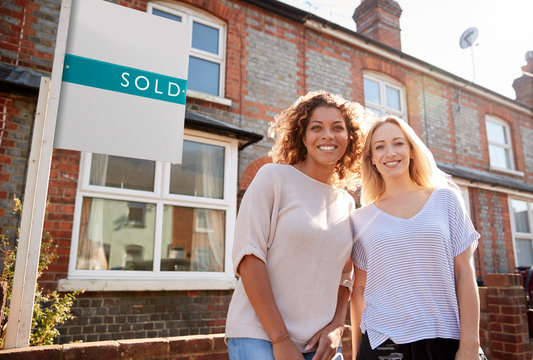 Portrait Of Two Women Standing Outside New Home With Sold Sign