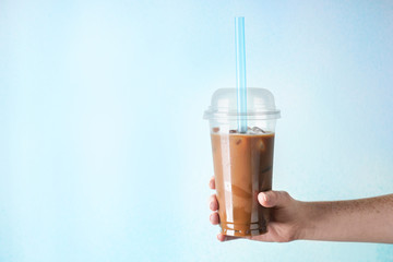 Female hand with plastic cup of tasty frappe coffee on color background