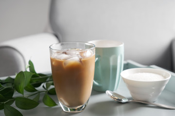 Glass of tasty frappe coffee and bowl with sugar on table