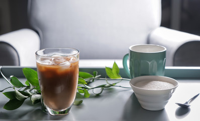 Glass of tasty frappe coffee and bowl with sugar on table