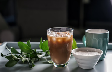 Glass of tasty frappe coffee and bowl with sugar on table